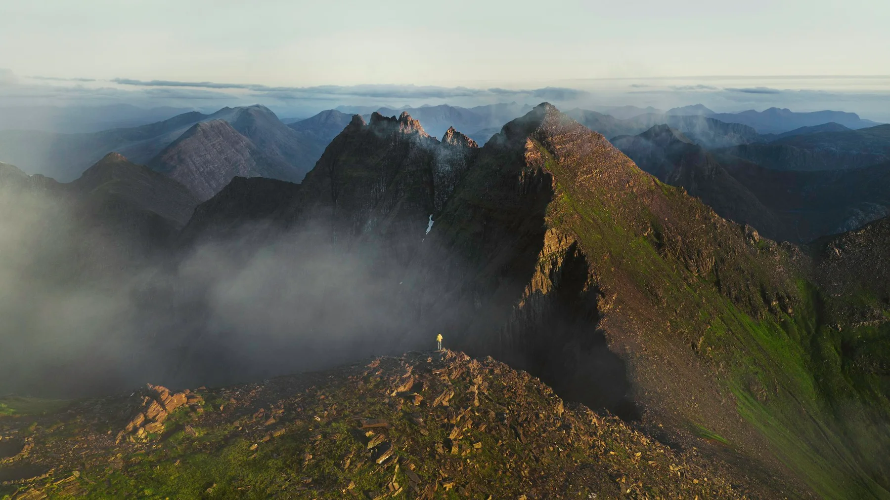 Un caminante solitario contempla las montañas desde una cresta rocosa en Escocia